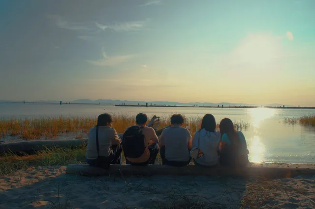 Friends sitting together on a log facing the ocean at sunset